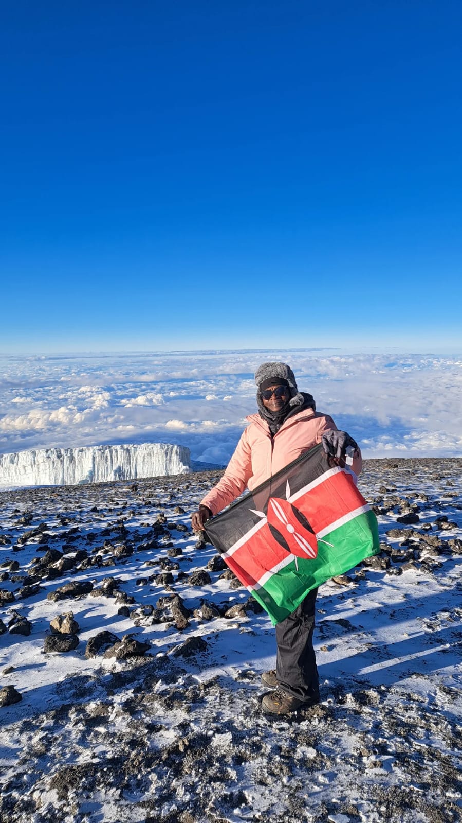Rtn. Lydia Kimundu holding a Kenyan flag on a mountain